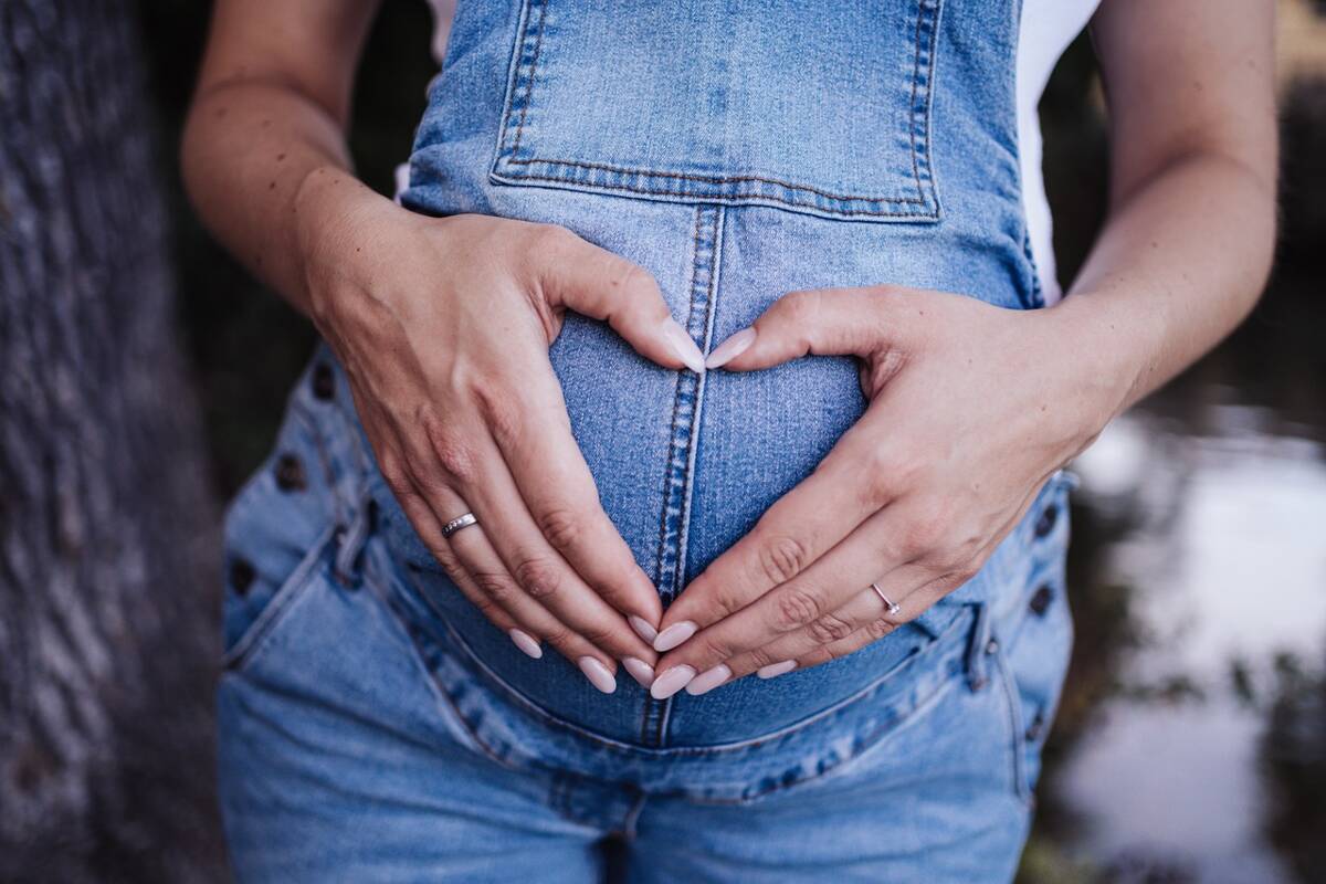 Schwangere in Jeanshose und Hände Herz am Bauch